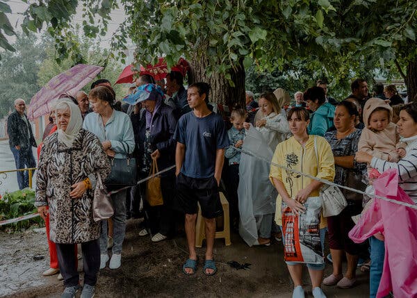 A group of people in Russia stand by a tree as they wait for distribution of aid.